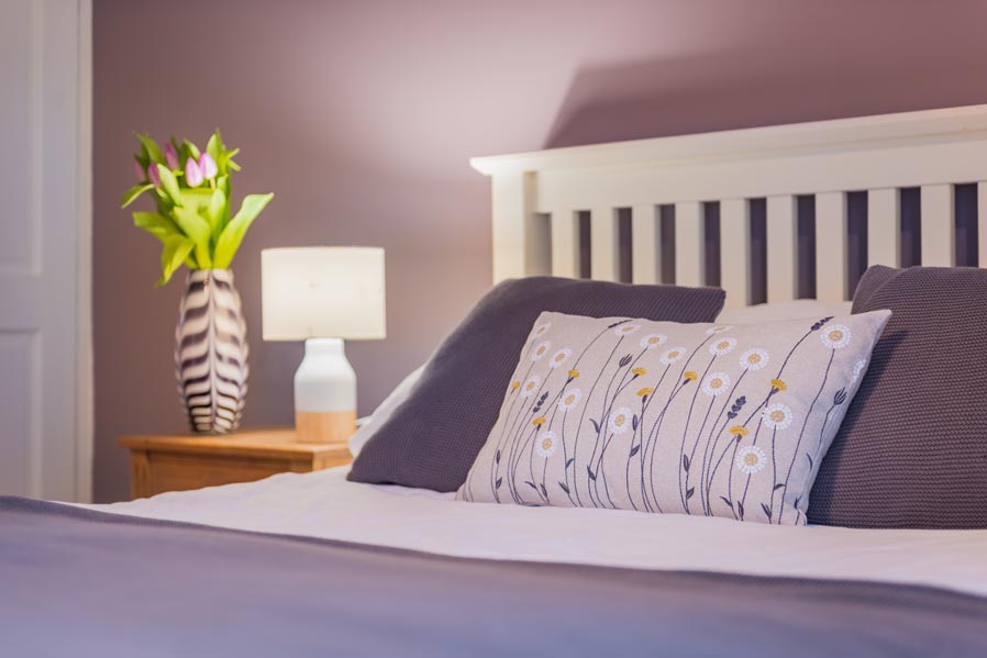 Double bedroom detail with floral cushion and bedside flowers